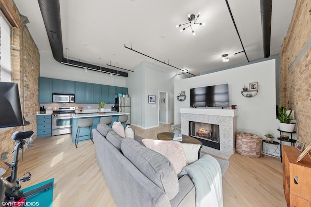 living area featuring light wood-type flooring, brick wall, and a fireplace with flush hearth