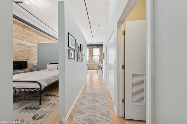 hallway with light wood finished floors, visible vents, attic access, brick wall, and baseboards