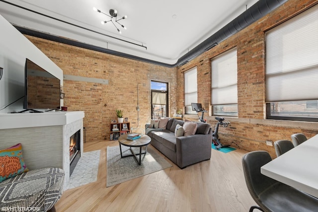 living room with a fireplace with flush hearth, a high ceiling, brick wall, and wood finished floors