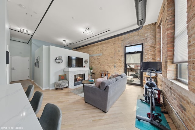 living area featuring a glass covered fireplace, baseboards, light wood-style flooring, and brick wall