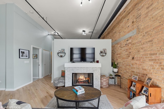 living area with a towering ceiling, light wood finished floors, brick wall, and a tile fireplace