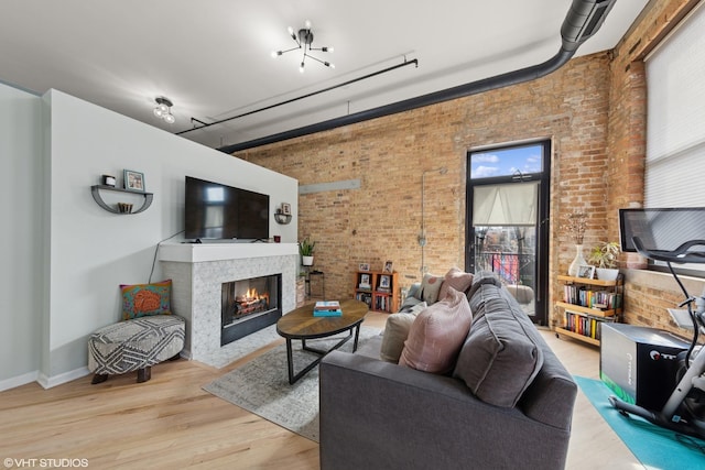 living room featuring brick wall, baseboards, a tiled fireplace, and wood finished floors