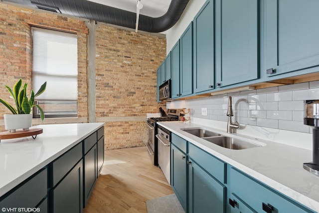 kitchen with light wood-style flooring, brick wall, stainless steel appliances, a sink, and light countertops