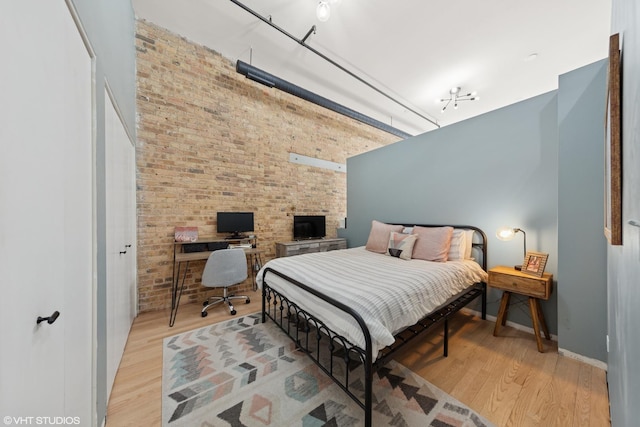 bedroom with a towering ceiling, brick wall, baseboards, and wood finished floors