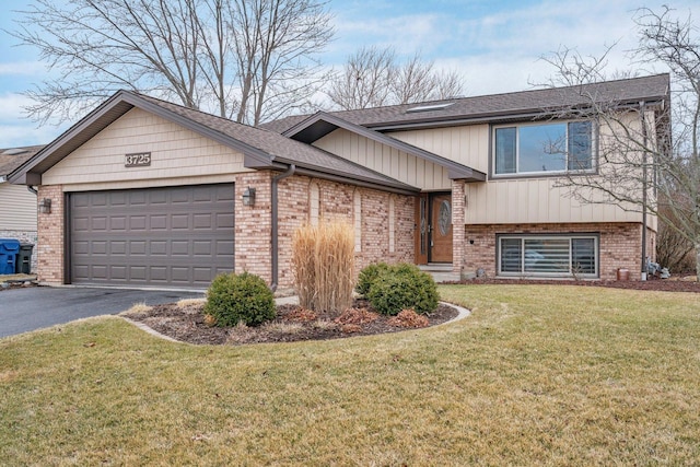 split level home with a shingled roof, aphalt driveway, an attached garage, a front yard, and brick siding