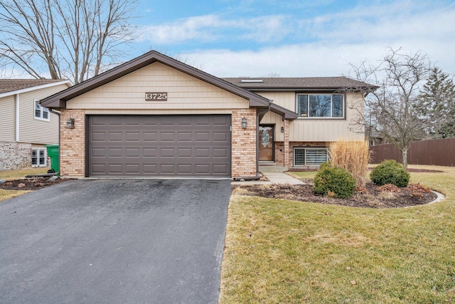 split level home featuring brick siding, fence, a garage, driveway, and a front lawn