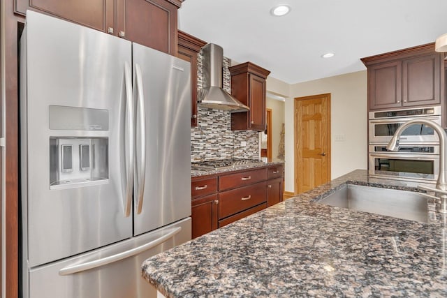 kitchen with recessed lighting, stainless steel appliances, a sink, decorative backsplash, and wall chimney exhaust hood