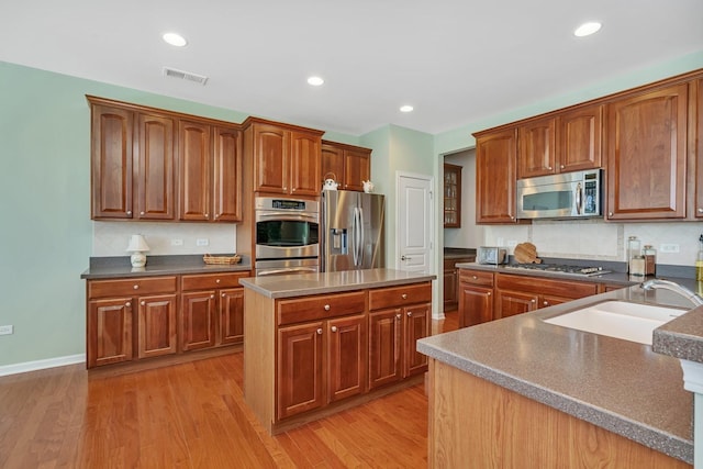 kitchen with light wood finished floors, a kitchen island, stainless steel appliances, a sink, and recessed lighting