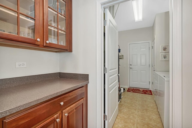 interior space with washer and clothes dryer, dark countertops, glass insert cabinets, brown cabinets, and light tile patterned flooring