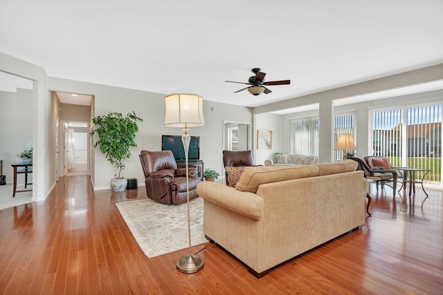 living room with a ceiling fan, baseboards, and wood finished floors