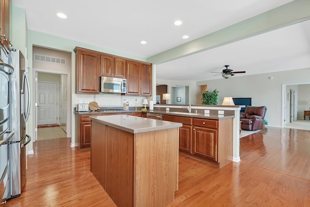 kitchen with stainless steel appliances, light wood-style floors, open floor plan, a kitchen island, and a peninsula