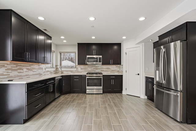 kitchen with stainless steel appliances, recessed lighting, tasteful backsplash, light countertops, and a sink