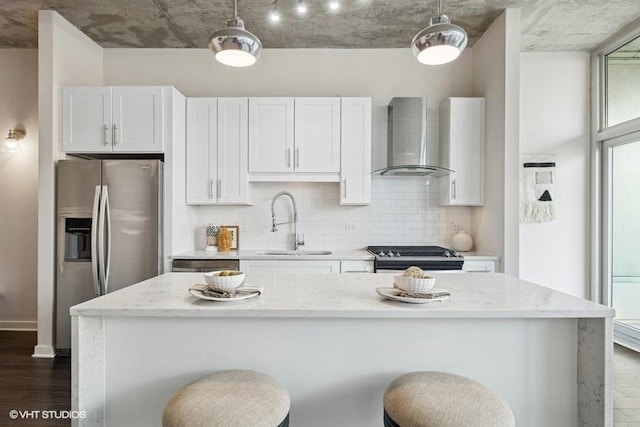 kitchen featuring stainless steel appliances, backsplash, white cabinets, a sink, and wall chimney exhaust hood