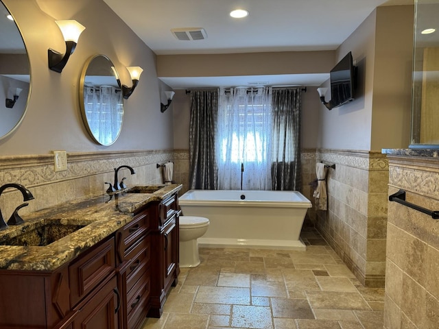 bathroom with a freestanding bath, wainscoting, a sink, and stone tile flooring