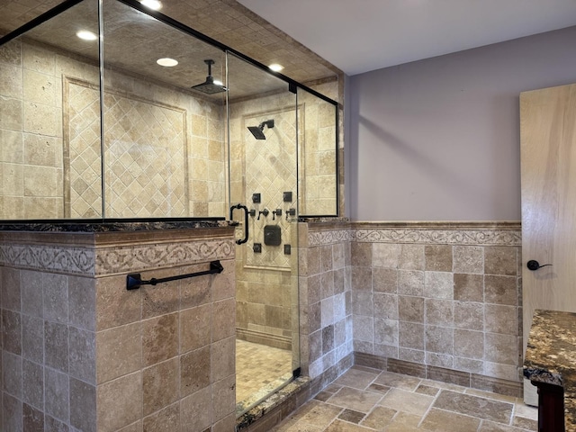 bathroom with recessed lighting, a wainscoted wall, tile walls, a stall shower, and stone tile flooring