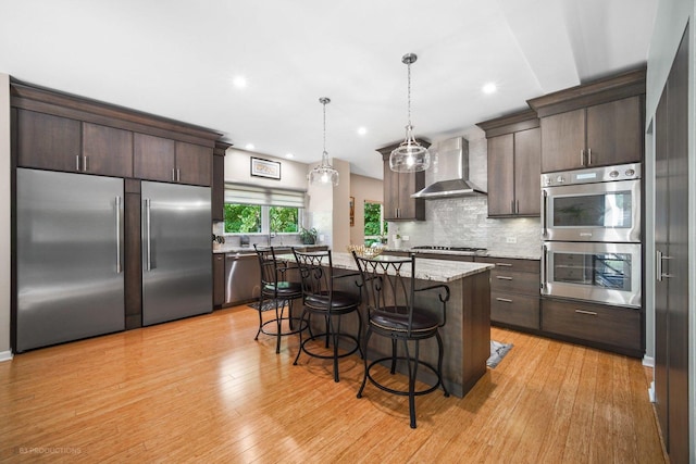 kitchen featuring dark brown cabinetry, wall chimney range hood, a breakfast bar, and stainless steel appliances