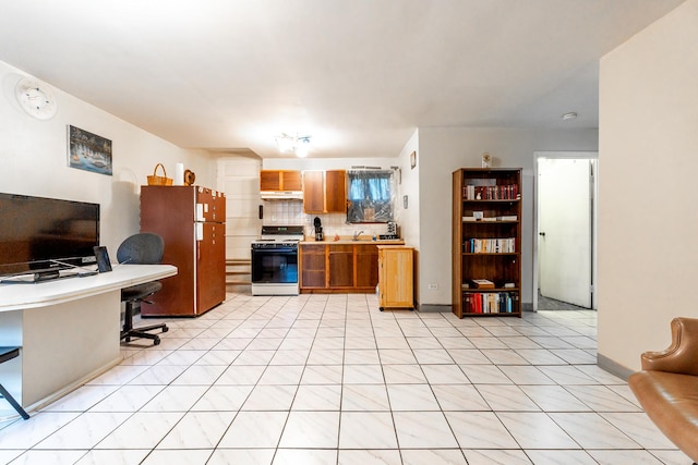 kitchen with under cabinet range hood, light countertops, freestanding refrigerator, brown cabinetry, and range with gas cooktop