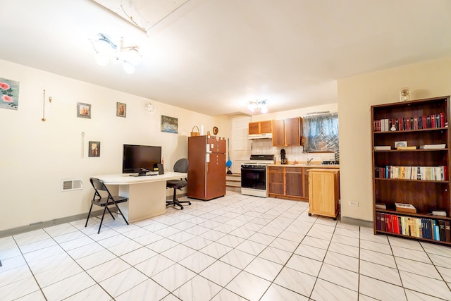 kitchen with range with gas stovetop, freestanding refrigerator, light countertops, a kitchen bar, and backsplash