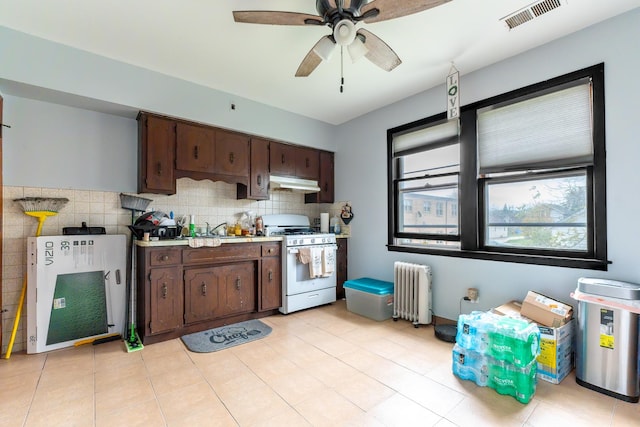 kitchen featuring white gas stove, under cabinet range hood, visible vents, dark brown cabinets, and radiator heating unit