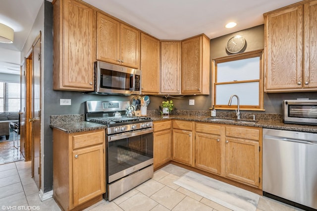 kitchen with recessed lighting, appliances with stainless steel finishes, light tile patterned flooring, a sink, and dark stone countertops