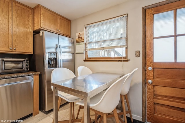 kitchen with stainless steel appliances, a toaster, brown cabinetry, and light tile patterned floors