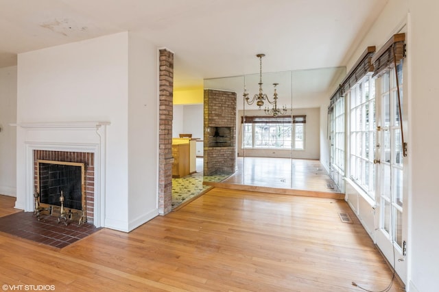 interior space featuring an inviting chandelier, a fireplace, visible vents, and wood finished floors