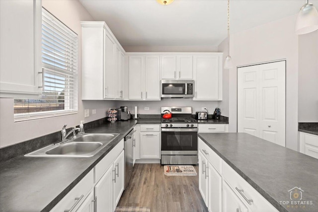 kitchen featuring a sink, dark countertops, wood finished floors, appliances with stainless steel finishes, and white cabinets