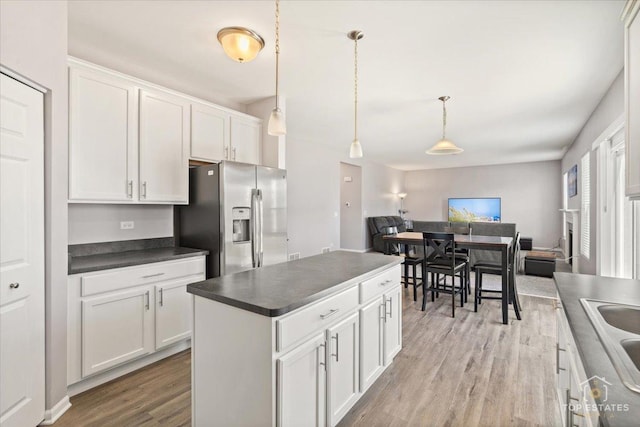 kitchen featuring dark countertops, open floor plan, light wood-style floors, stainless steel refrigerator with ice dispenser, and white cabinets