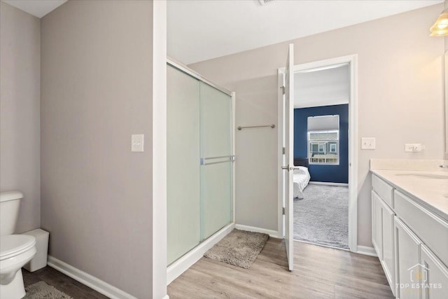 ensuite bathroom with vanity, toilet, wood finished floors, and a stall shower