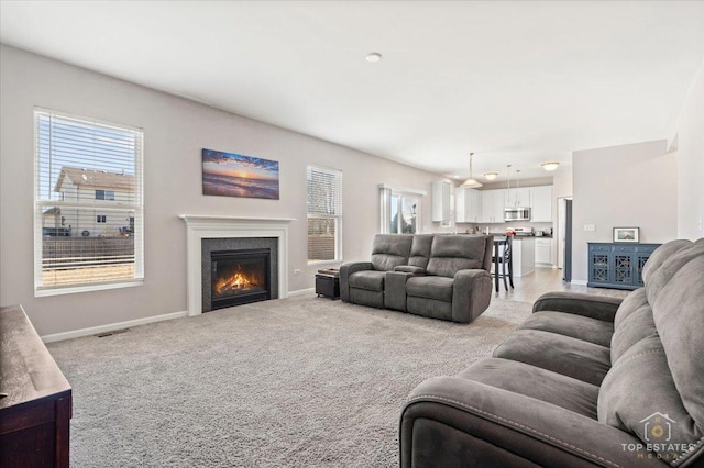 living room with a glass covered fireplace, visible vents, baseboards, and light carpet