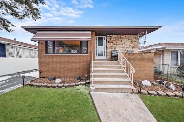 view of front of house featuring a front yard, stone siding, brick siding, and fence