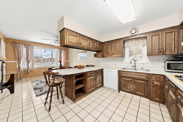 kitchen with light countertops, stainless steel microwave, a sink, dishwasher, and a peninsula