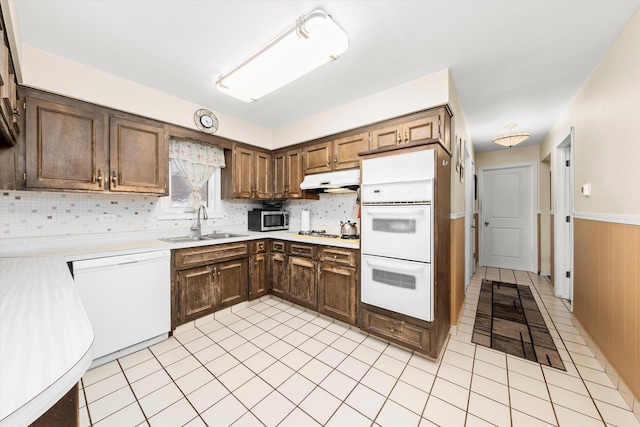 kitchen featuring white appliances, under cabinet range hood, light countertops, and a sink