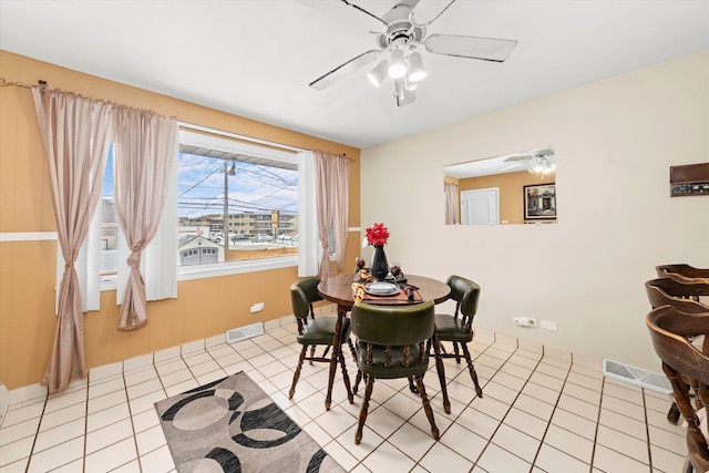 dining room with light tile patterned floors, ceiling fan, wood walls, and visible vents