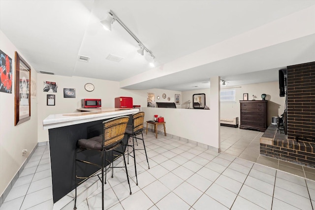 interior space with light tile patterned floors, visible vents, open floor plan, track lighting, and a kitchen breakfast bar