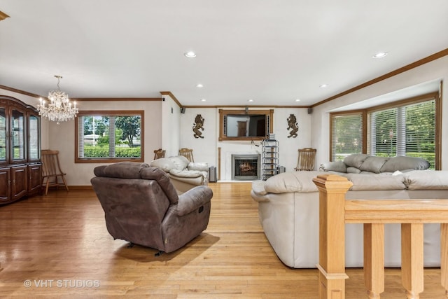 living area featuring recessed lighting, light wood-style floors, ornamental molding, a chandelier, and a warm lit fireplace