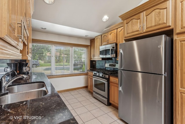 kitchen with light tile patterned floors, a sink, appliances with stainless steel finishes, dark stone counters, and tasteful backsplash