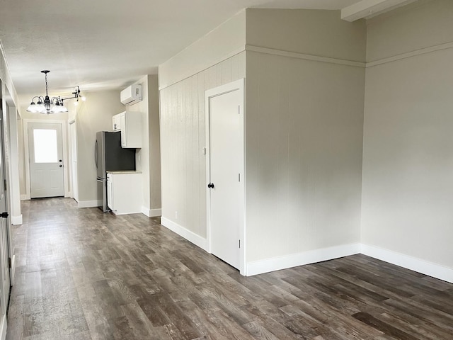 unfurnished room with baseboards, an AC wall unit, dark wood-style flooring, and a notable chandelier