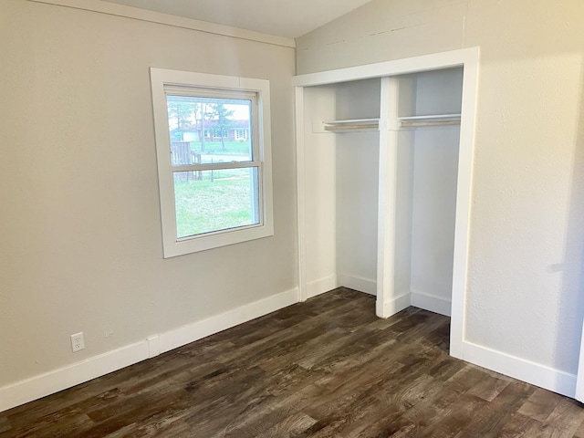 unfurnished bedroom featuring lofted ceiling, baseboards, dark wood finished floors, and a closet