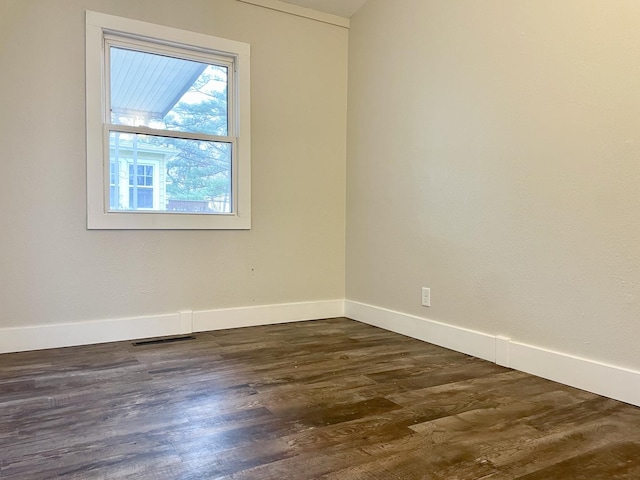 spare room featuring dark wood-type flooring, visible vents, and baseboards