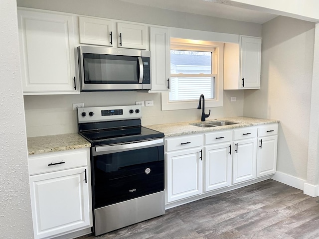 kitchen with appliances with stainless steel finishes, white cabinetry, a sink, wood finished floors, and baseboards