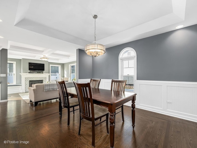 dining room with beam ceiling, a wainscoted wall, dark wood finished floors, a fireplace, and coffered ceiling