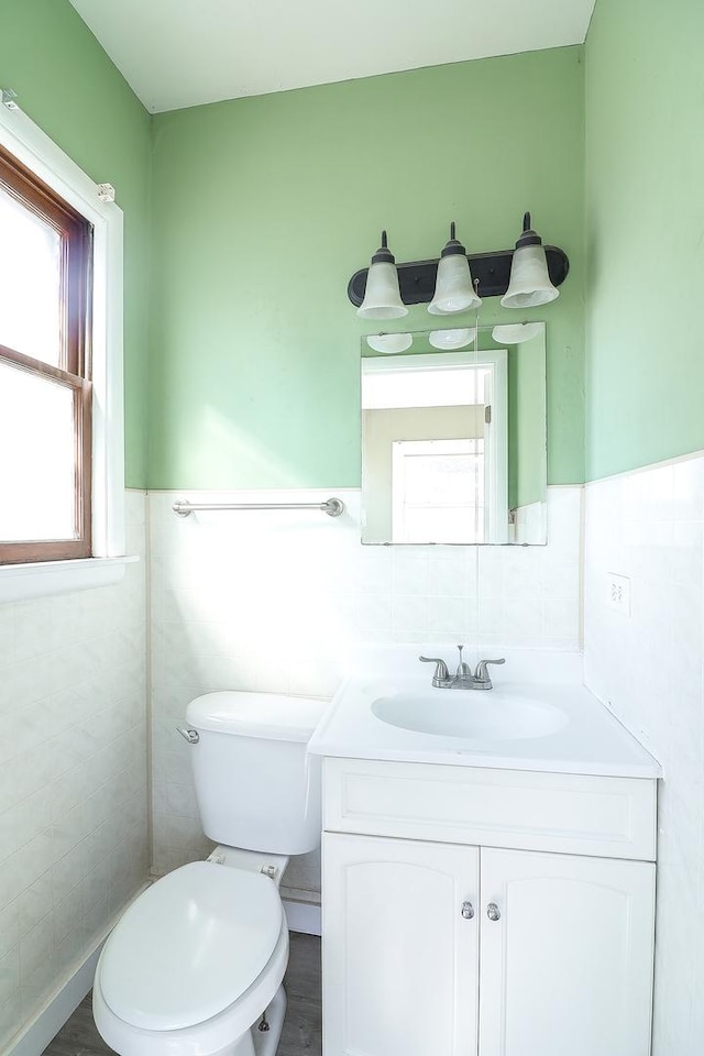 half bath featuring vanity, tile walls, toilet, and wainscoting