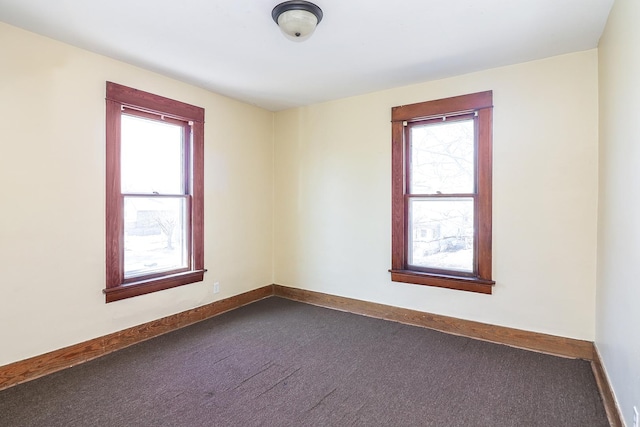 spare room featuring a wealth of natural light, baseboards, and dark carpet