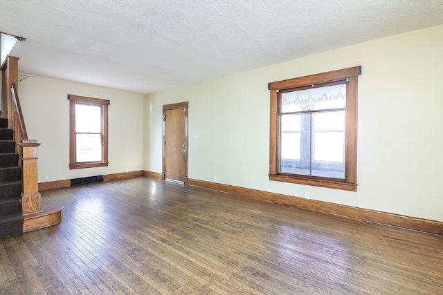 unfurnished living room featuring hardwood / wood-style floors, stairway, visible vents, and a textured ceiling