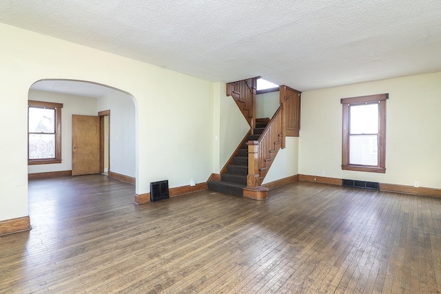 unfurnished living room with dark wood-type flooring, visible vents, arched walkways, and a wealth of natural light