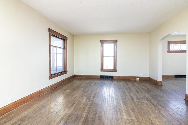 unfurnished room with arched walkways, visible vents, baseboards, and hardwood / wood-style flooring