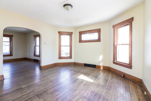 spare room featuring baseboards, arched walkways, plenty of natural light, and dark wood-style flooring