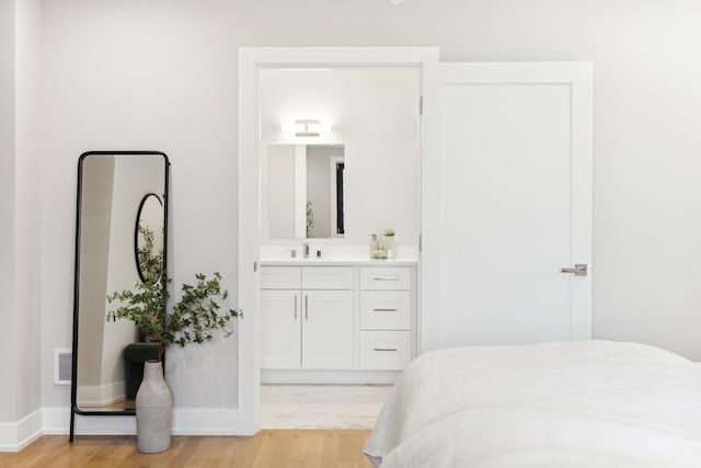 bedroom featuring visible vents, light wood-style floors, connected bathroom, a sink, and baseboards