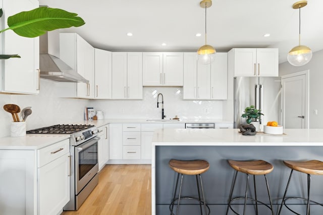 kitchen with a breakfast bar, a sink, white cabinets, wall chimney range hood, and appliances with stainless steel finishes